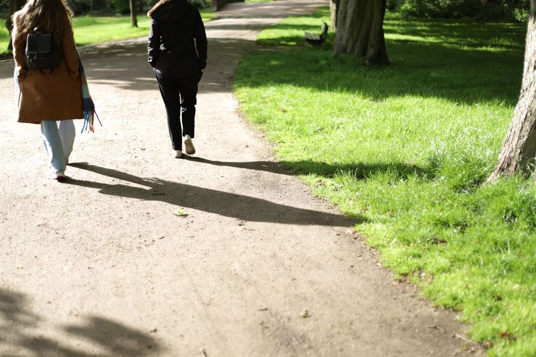 Two people walking together along a sunlit park path, deep in conversation